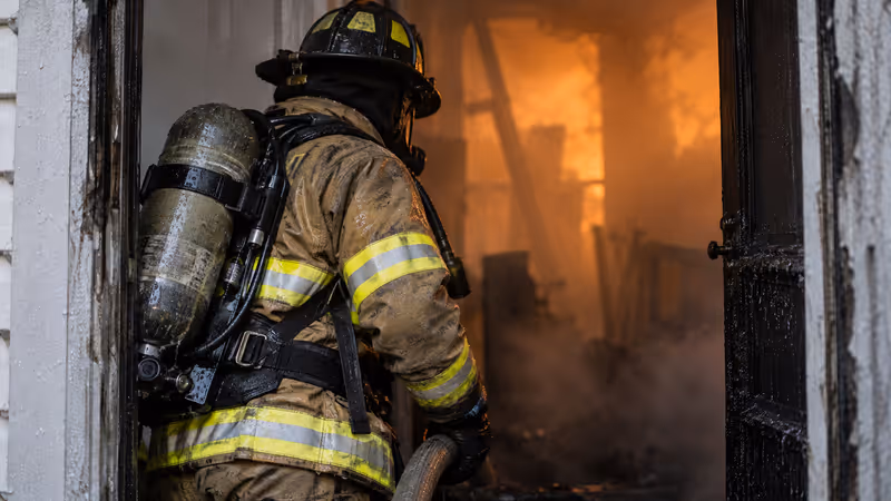 Bombero con traje estructural de tres capas y equipo de respiración frente a la entrada de un inmueble con humo